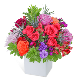 Mixed bouquet of roses and other flowers in a white square vase