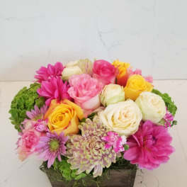 Mixed pink, yellow, and white flowers arranged in a rectangular wooden box