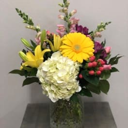 Mixed bouquet with yellow lilies, white hydrangea, and pink flowers in a glass vase