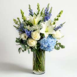 Bouquet of white lilies, cream roses, blue hydrangea, and purple flowers in a glass vase