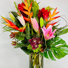Tropical bouquet with pink lilies, orchids, and orange heliconia in a glass vase