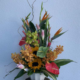 Tall tropical arrangement with orchids, sunflowers, and anthuriums in a white vase