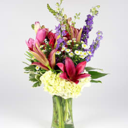 Colorful bouquet of lilies, hydrangea, and purple spikes in a glass vase