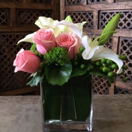 Pink roses and white lilies arranged in a square glass vase