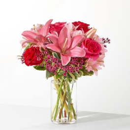Pink lilies and red roses arranged in a clear glass vase.