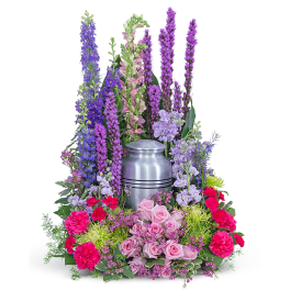 Colorful funeral urn arrangement with pink roses and tall purple flowers