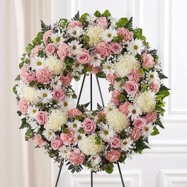Pink and white floral wreath on a black stand