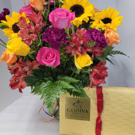 Mixed bouquet with sunflowers, roses, and alstroemeria beside a Godiva chocolate box