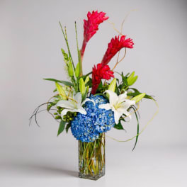 Tall vase arrangement with blue hydrangea, white lilies, and red tropical blooms