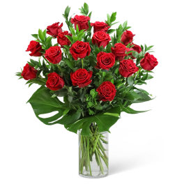 Red roses arranged in a clear glass vase with broad green leaves