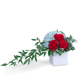 Red roses and blue hydrangeas in a white square vase