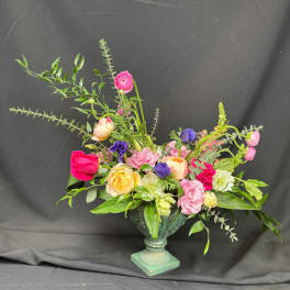 Mixed bouquet of pink, yellow, purple, and white flowers in a decorative urn vase