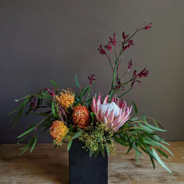 Arrangement of pink protea and orange pincushion blooms in a black vase