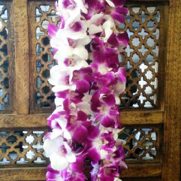 Purple and white orchid lei draped over a carved wooden panel