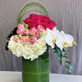 Pink roses, white hydrangeas, and white orchids in a green vase