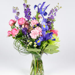 Mixed bouquet of pink, purple, and blue flowers in a clear glass vase