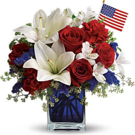 Red roses and white lilies in a blue glass vase with a small American flag