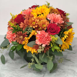 Mixed bouquet of sunflowers, roses, and carnations in a low container