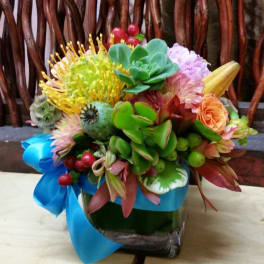 Colorful bouquet with succulents and mixed flowers in a glass vase tied with blue ribbon