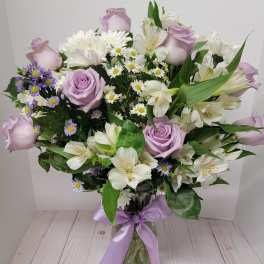 Lavender roses and white lilies in a glass vase with a purple ribbon