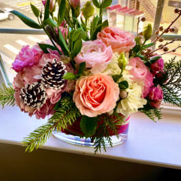 Pink and peach floral arrangement in a clear glass vase with pinecones