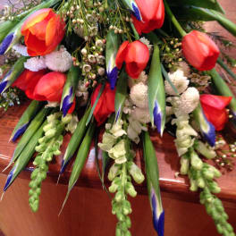 Loose bouquet of red tulips, blue-tipped iris, white flowers, and green snapdragons draped on a wooden surface