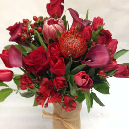 Red floral bouquet with roses, tulips, and calla lilies in a burlap-wrapped vase