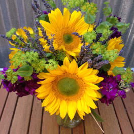 Bright sunflower arrangement with purple flowers in a clear glass vase on a wooden table