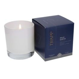 Lit white candle in a glass tumbler beside a navy product box