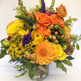 Bright mixed bouquet of orange, yellow, and purple flowers in a glass vase