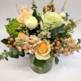 Low arrangement of peach and cream roses with mixed blooms in a clear glass vase