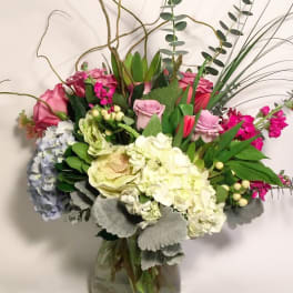 Mixed bouquet of pink roses, hydrangeas, and white blooms in a glass vase
