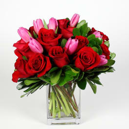 Red roses and pink tulips in a clear glass vase