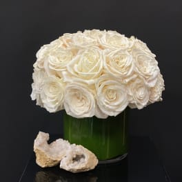 White rose bouquet in a green glass vase with two crystal rocks in front