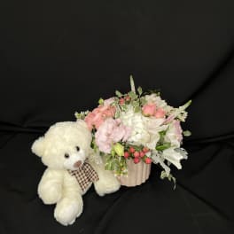 White teddy bear beside a pink floral arrangement in a ribbed vase
