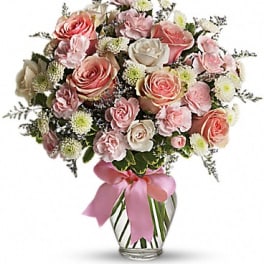 Pink and white rose bouquet in a clear glass vase with a pink ribbon