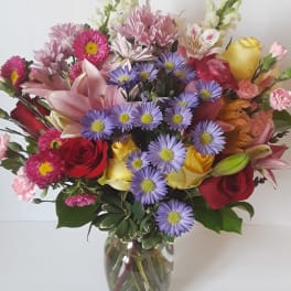 Mixed bouquet of roses, lilies, and purple daisies in a glass vase