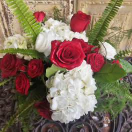 Red roses and white hydrangeas arranged with fern fronds