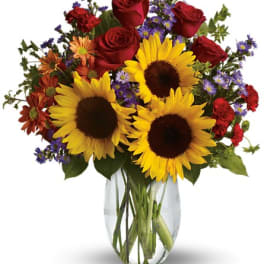 Bouquet of red roses, sunflowers, and mixed daisies in a clear glass vase