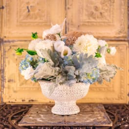 White and pale blue floral arrangement in a decorative pedestal vase