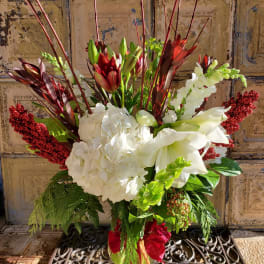 Tall floral arrangement with white hydrangeas, lilies, and red accents in a vase