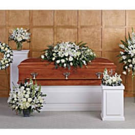White funeral casket surrounded by white floral sprays and wreaths