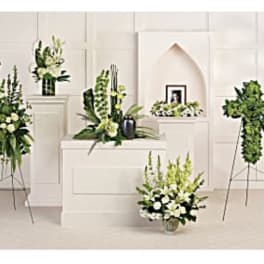 Multiple white and green floral funeral arrangements on stands and pedestals