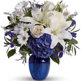 White lilies and daisies arranged in a blue vase with purple accents
