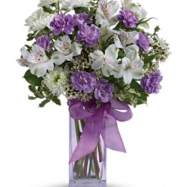 Purple and white bouquet in a clear glass vase with a ribbon