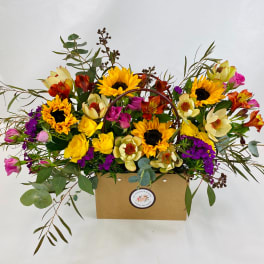 Mixed bouquet with sunflowers, roses, and purple blooms in a kraft box