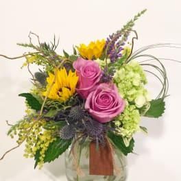 Mixed bouquet with pink roses, sunflowers, and green hydrangea in a glass vase