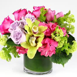 Pink roses and orchids in a glass vase with green accents