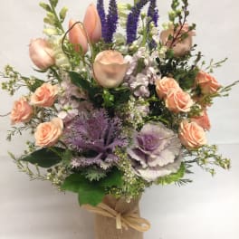 Peach roses and purple flowers arranged in a burlap-wrapped vase