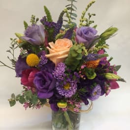 Mixed bouquet of purple, peach, and pink flowers in a glass vase